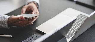 Geschäftsmann mit Handy in der Hand vor dem Laptop