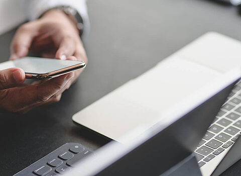 Geschäftsmann mit Handy in der Hand vor dem Laptop