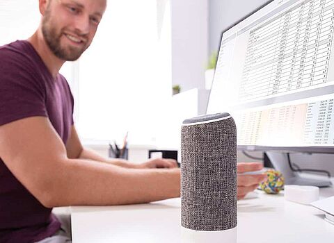 Mann sitzt vor seinem Computer und spricht mit seinen Voice Assistent
